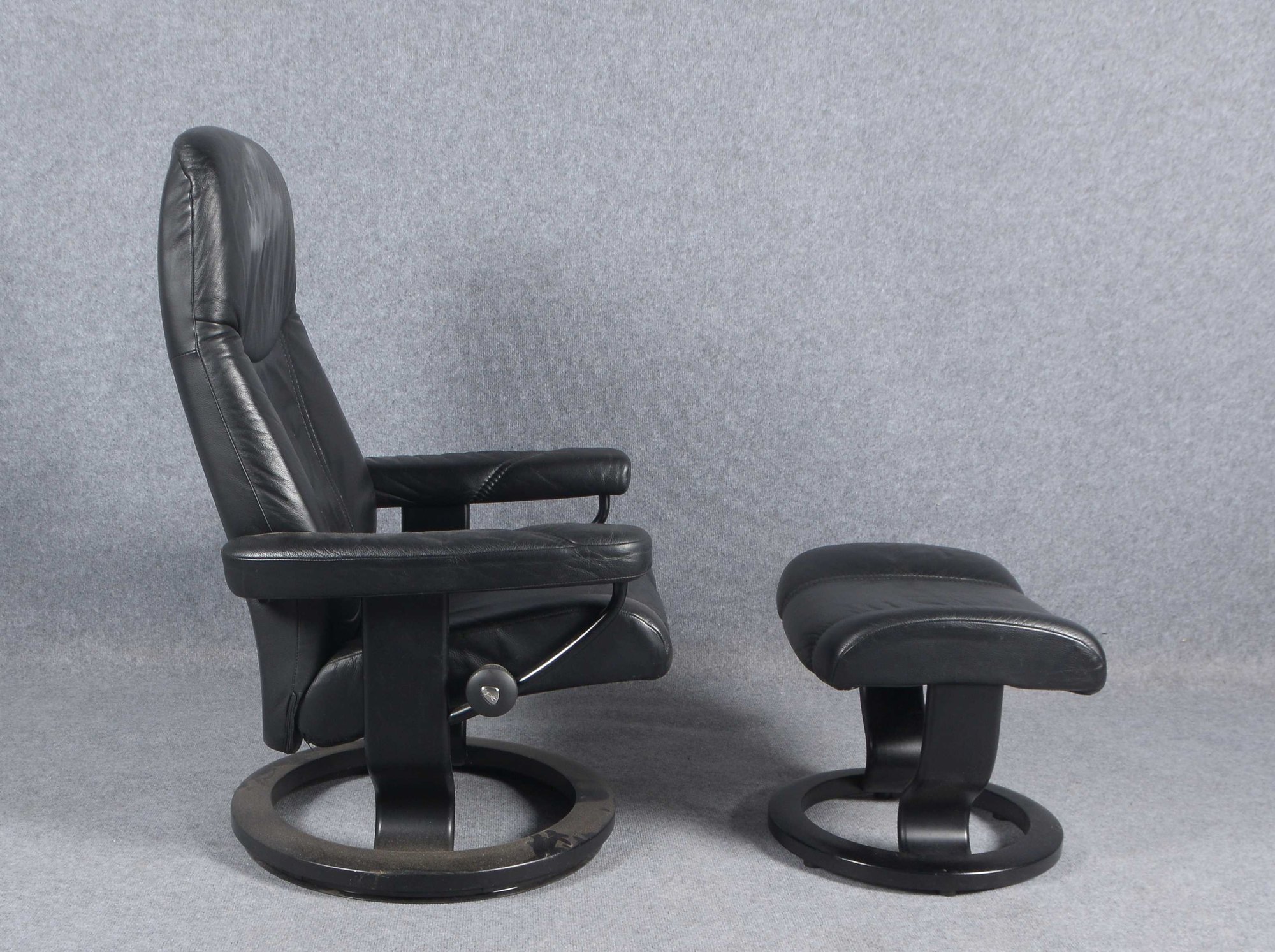 Stressless-Sessel, schwarzes Leder, auf rundem drehbarem Fuß, mit Hocker