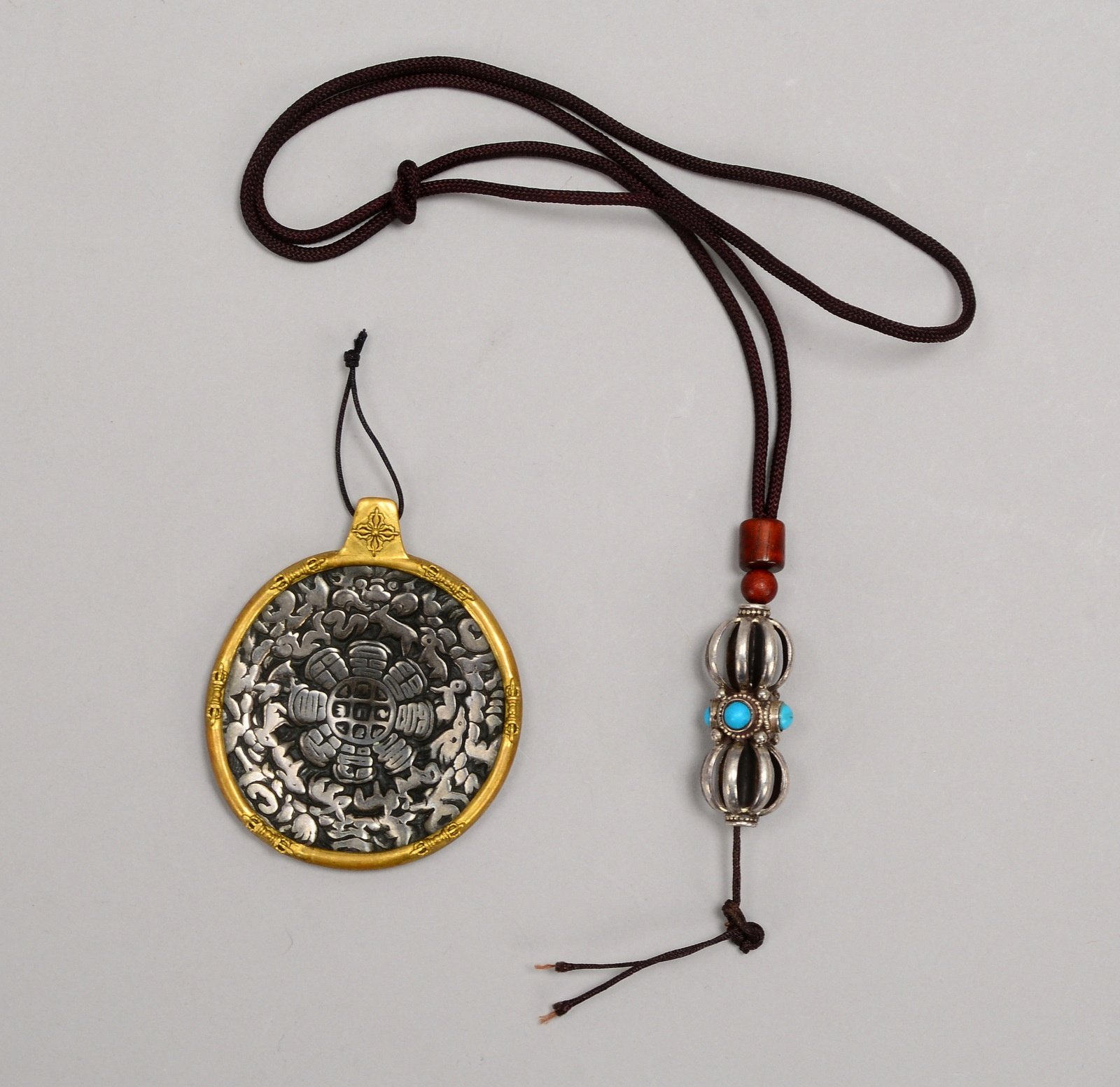 2 Anhänger: 1x Vajra-Anhänger, Silber; 1x Amulett-Anhänger, Bronze, mit Reliefdekor