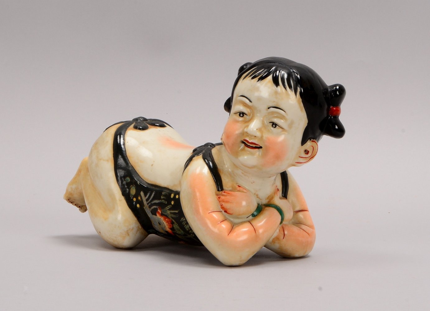 Porzellanfigur, 'Liegendes Kind', polychr. Handbemalung, unters. mit Glücksmotiven