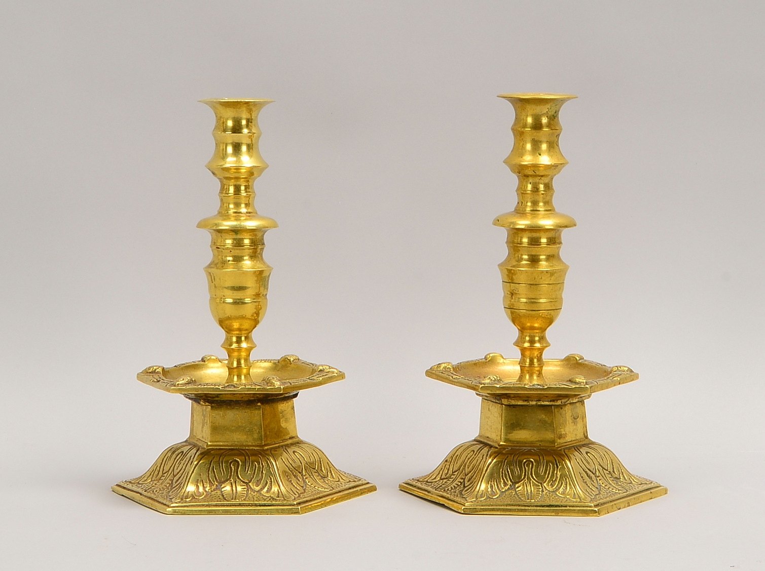 2 Glockenfuß-Leuchter (17. Jh.), Messing, 6-eck. Stand/Traufschale mit 'Cherub.', profil. Schaft