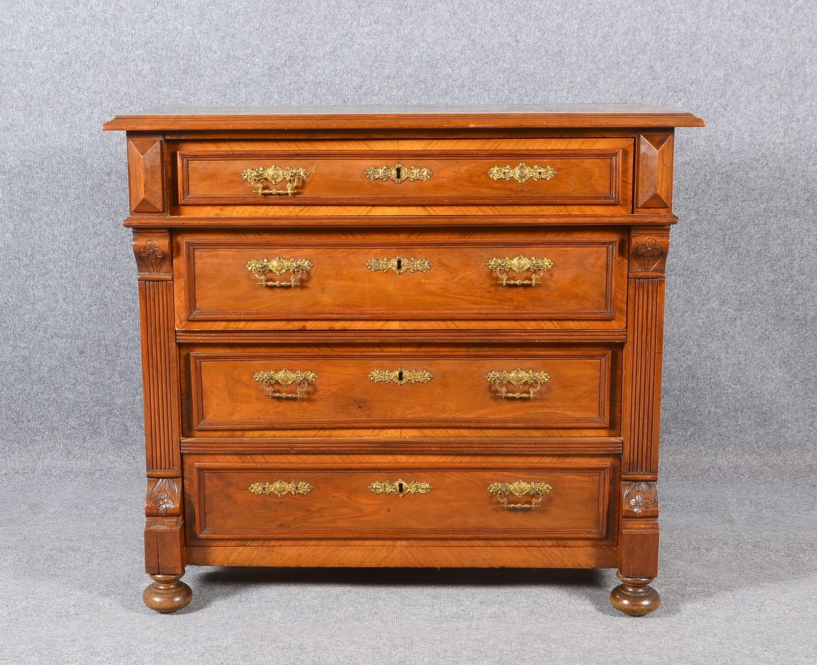 Kommode, Nussbaum furn., 4-schübig, seitl. Pilaster/Schnitzwerk, Messingbeschl.