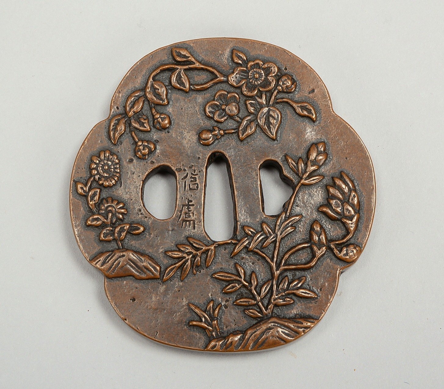 Bronze-Tsuba, Wandung mit floralem Reliefdekor und japan. Inschrift; Maße 8,5 x 8 cm