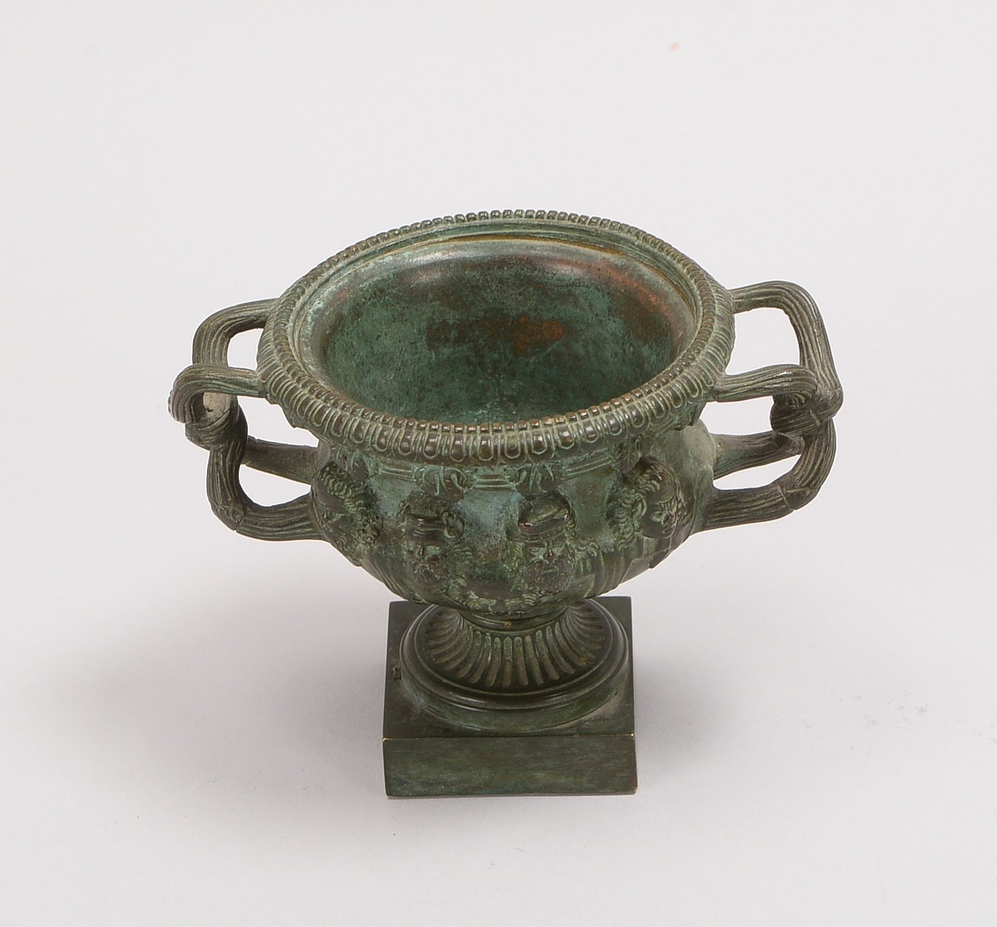 Kratervase, Bronze/grün pat., 8x plast. Köpfe, 2x Handhaben, Fuß gefüllt!; Höhe 9,5 cm