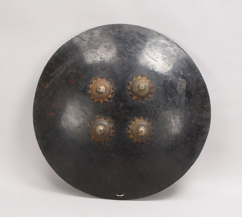 Dhal/Rundschild, schwarz gefasstes Leder, 4x Metallbuckel, innen 2x Kordeln/Kissen